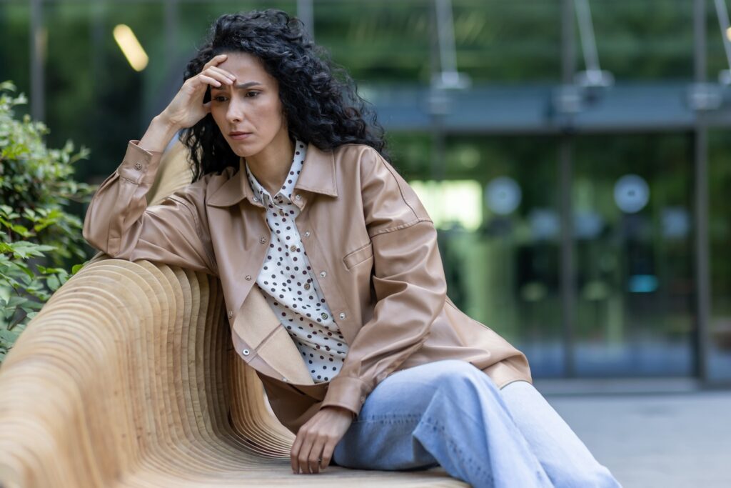 A woman sitting on a bench outside an office building, looking upset. Navigating mood shifts during perimenopause can be difficult, and a perimenopause depression treatment in Park Ridge can help.
