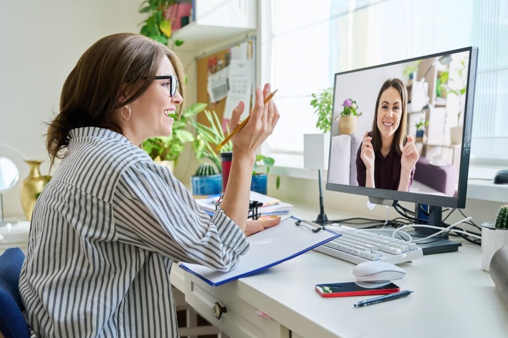 A mature woman sits at a desk with her desktop during a telehealth appointment. She is meeting with her therapist to discuss her perimenopause depression treatment in Park Ridge.