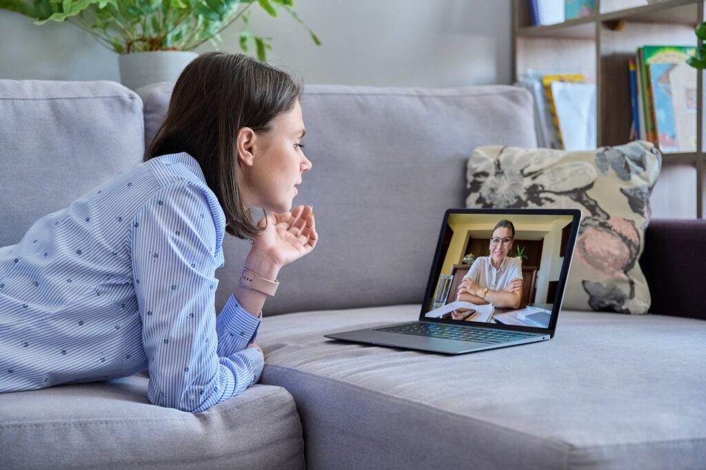A woman lies on her couch with her laptop during a telehealth appointment. She is meeting with her therapist to discuss her prenatal depression treatment in Park Ridge.