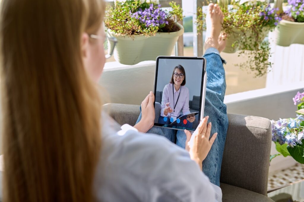 A woman sits with a tablet on her lap during a telehealth appointment. She is meeting with her therapist to discuss her cognitive behavioral therapy for postpartum depression in Park Ridge.
